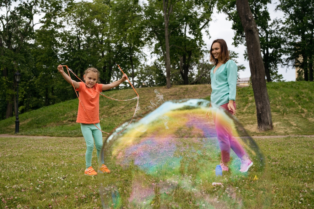 Mergaitė su mama pučia labai didelius muilo burbulus